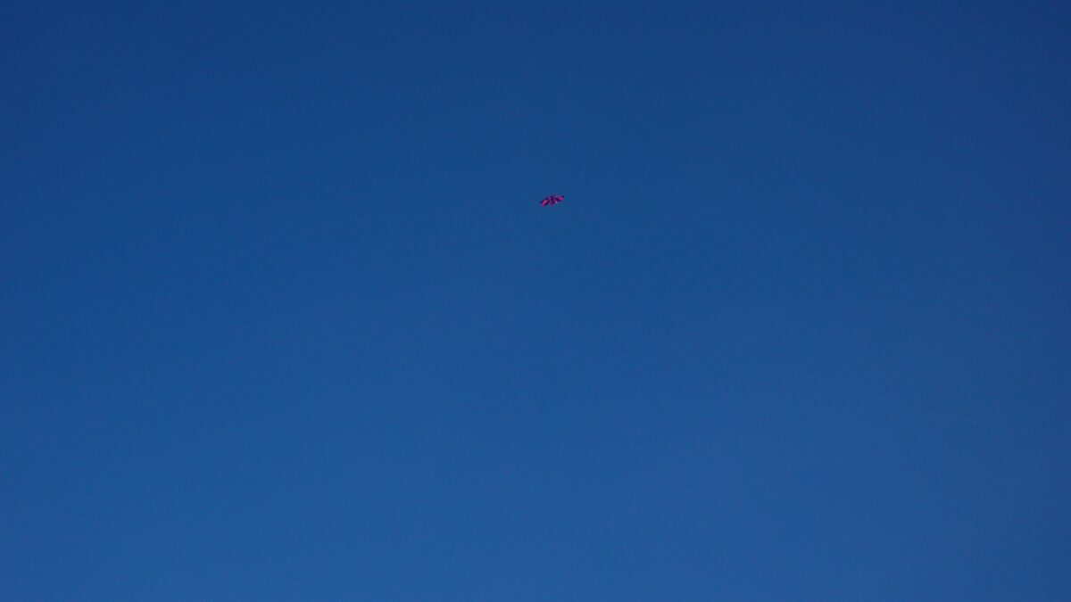 tiefblauer himmel, man sieht oben in der mitte einen winzigen roten kinderdrachen fliegen