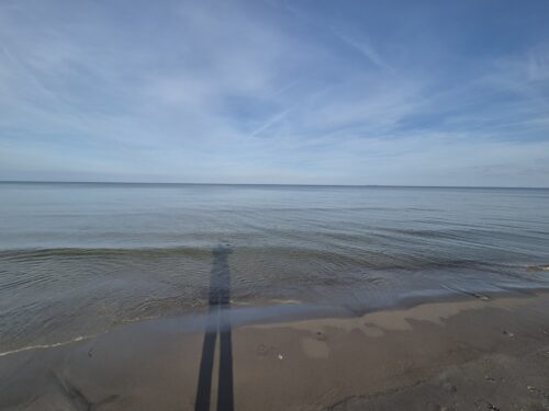 blick auf die ostsee, man sieht den langen schatten eines menschen am wasser